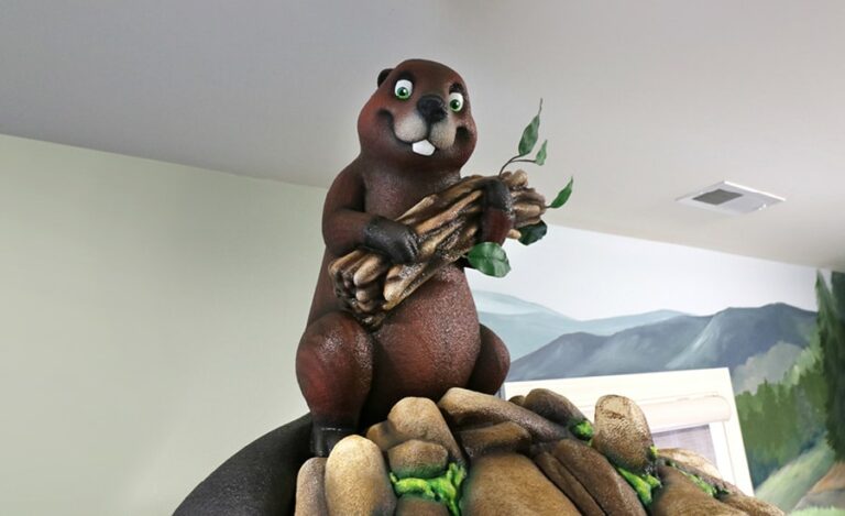 Perched sculpted beaver holding a bundle of sticks.