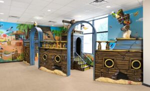 Enclosed kid's play corner in dental office with pirate ship themed walls, sculpted pirate animal characters and yellow slide