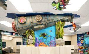 Side profile of a sculpted submarine with custom lighting, an octopus character and seaweed decor with underwater murals