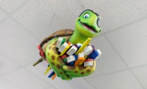 Swimming turtle character hanging from ceiling holding a bundle of colorful toothbrushes