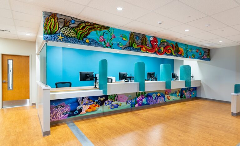 dental reception desk with underwater-themed murals and desk cladding in family-friendly medical clinic