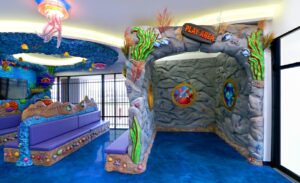 enclosed kids play area with sculpted rocky wall surrounds next to a dental office waiting room with sand and blue coral custom seating