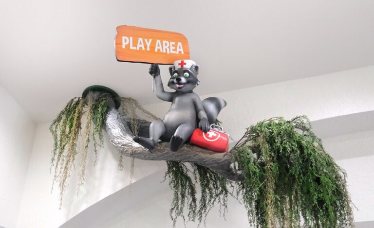 Cute sculpture of raccoon in nurse hat with medical bag sitting on tree branch coming from the ceiling