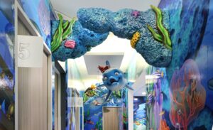 Dental practice hallway lined with underwater murals, hanging dolphin and turtle sculptures and a coral archway