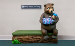 Sculpture of mama bear holding sick baby bear on custom log bench in medical office