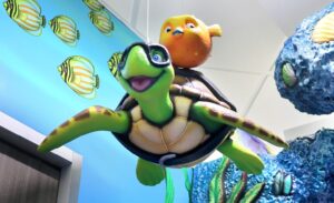 Smiling turtle with an orange pufferfish swim above a pediatric clinic hallway next to coral fixtures