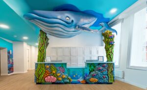 underwater themed reception desk with whale sculpture above, seaweed towers, and coral desk cladding in kids dentist office