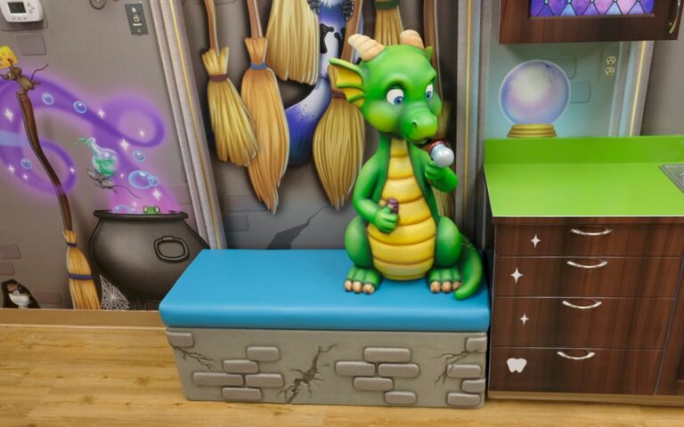 Bubble-blowing dragon character sitting on a castle-themed bench in a dental treatment room