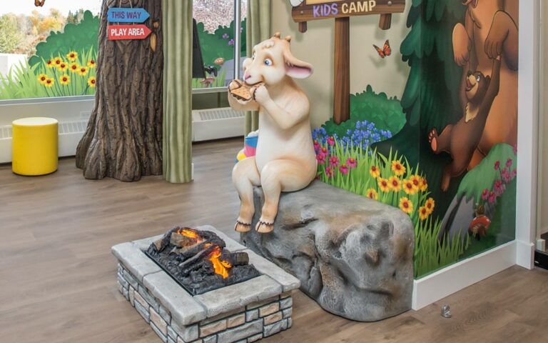 A goat character in front of a fire pit eating a smore.
