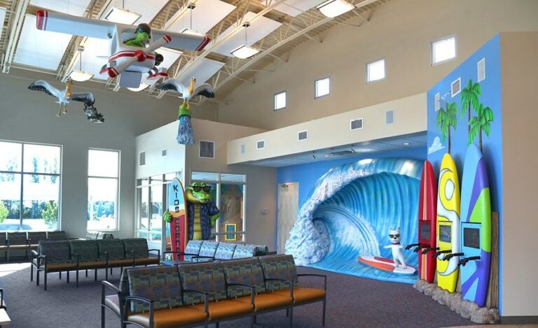 dentistry waiting area with giant sculpted wave flying birds overhead and surfboard themed gaming systems