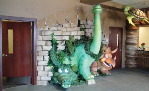 dinosaurs and alligator photo op sculpture bursting through faux brick wall