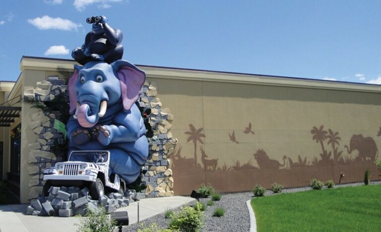 exterior sculpture of an elephant and gorilla driving through the wall in a jeep