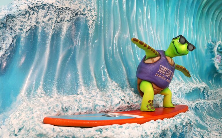 A turtle mascot riding a surfboard that children can pose on.