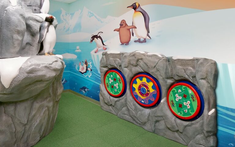 Keebee playboards for toddlers on a sculpted rock wall with a penguin mural in the background.