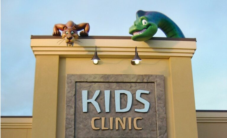 rooftop sculptures of a sabertooth tiger and dinosaur above exterior kids clinic sign
