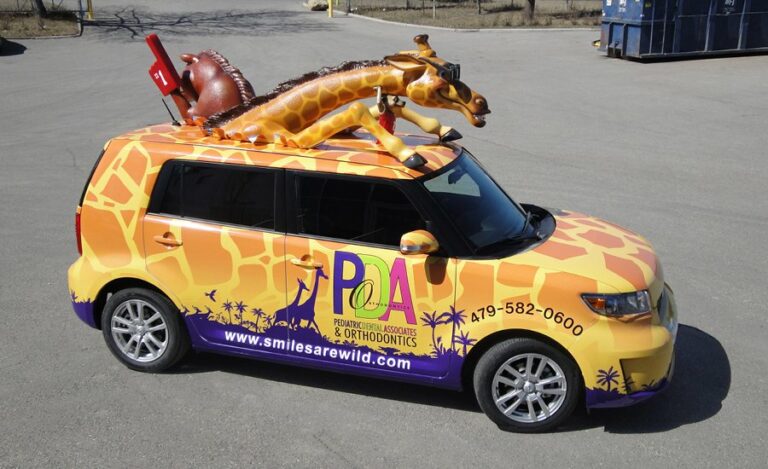 side view of a commercial car with giraffe spotted wrap and roof top safari animal mascots