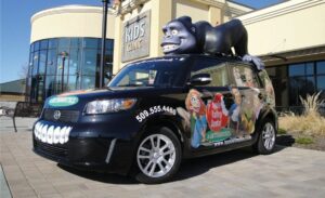 wrapped vehicle traveling billboard with with sculpted gorilla with braces on top of car
