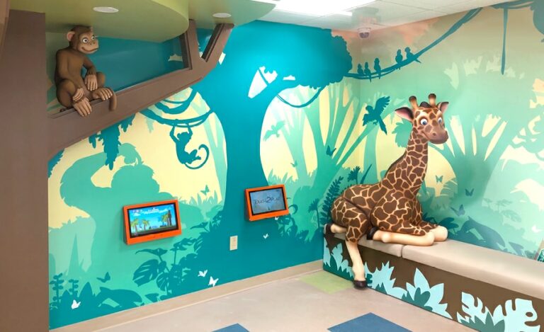 Jungle themed waiting room with a photo-op giraffe, sculpted monkey on a tree branch, and wall mounted gaming systems.