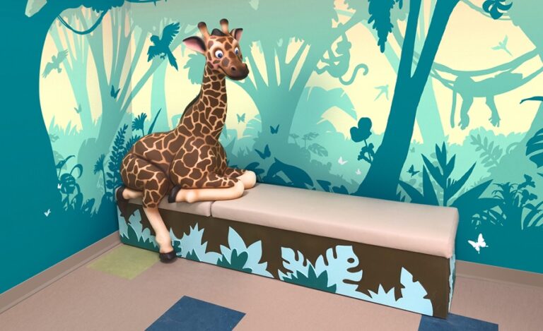Friendly photo-op giraffe perched on a cladded turquois, blue, and brown jungle theme bench.