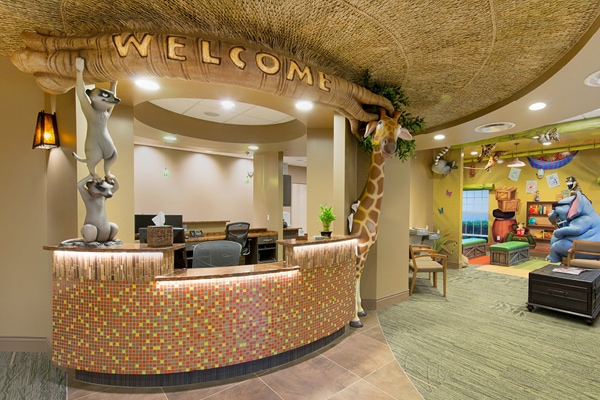 Safari themed reception desk with lemurs and a giraffe supporting a custom branch that reads 'welcome'.