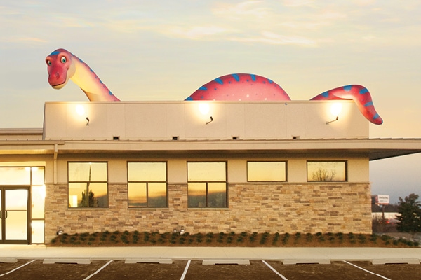 Exterior shot of business with a giant red and blue dinosaur landmark character on the roof.
