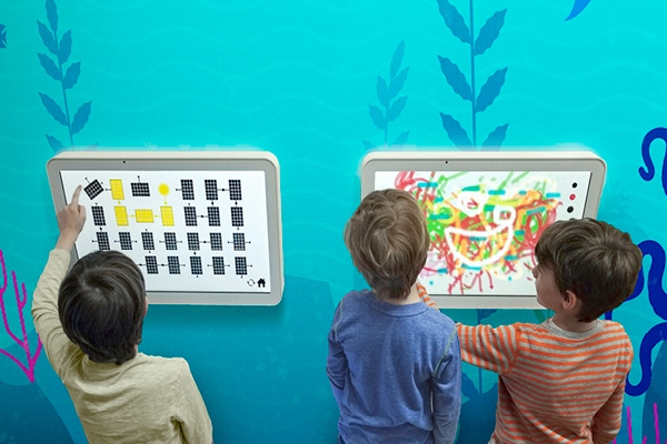 Kids playing on wall mounted gaming tablets.