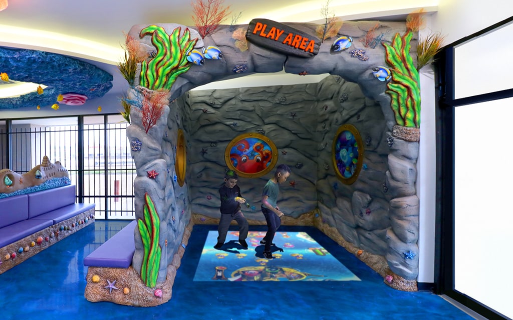 An underwater themed reception area with a sculpted cave featuring a floor projected video game for kids.