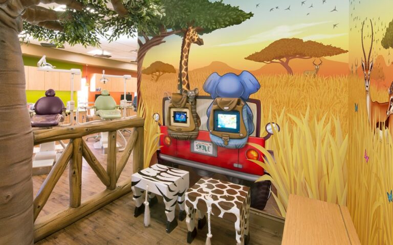 A gaming corner in a dental office treatment area, featuring a safari themed mural and 2 gaming tablets on the backs of an elephant and giraffe.