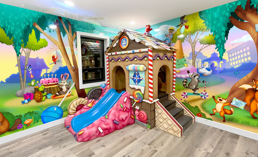 Candyland themed kid's play area with colorful wall murals and sculpted gingerbread house play structure with slide.